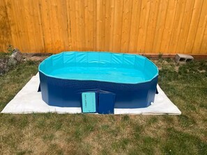 A blue inflatable pool on a white mat in a grassy yard with a wooden fence in the background. - Split King adjustable bed, fish pond and huge fenced in yard - 1 mile to CSU (Fort Collins)