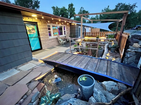 A patio area with a wooden deck, a small pond, and a stone wall.
