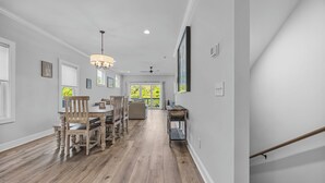 A spacious hallway with wooden flooring, a dining area with chairs and a table, a ceiling fan, and a staircase. - Golf Cart Included + Close to Beach and Restaurants! (Carolina Beach)