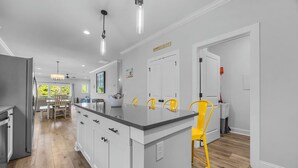 A modern kitchen with a central island, white cabinetry, and a yellow chair. - Golf Cart Included + Close to Beach and Restaurants! (Carolina Beach)