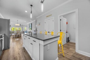 A modern kitchen with a central island, white cabinetry, and a yellow chair. - Golf Cart Included + Close to Beach and Restaurants! (Carolina Beach)