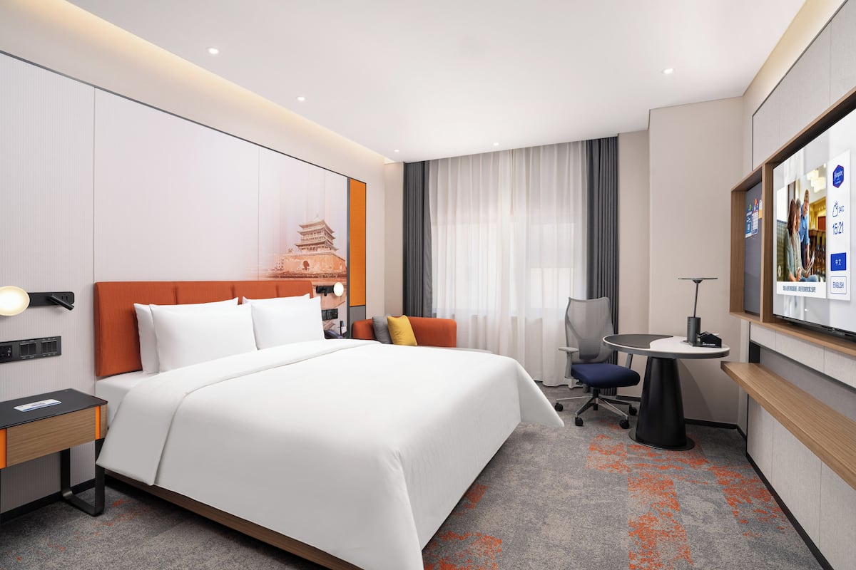 Une chambre d’hôtel équipée d’un lit, d’un bureau, d’une chaise, d’une télévision et d’une fenêtre avec des rideaux.