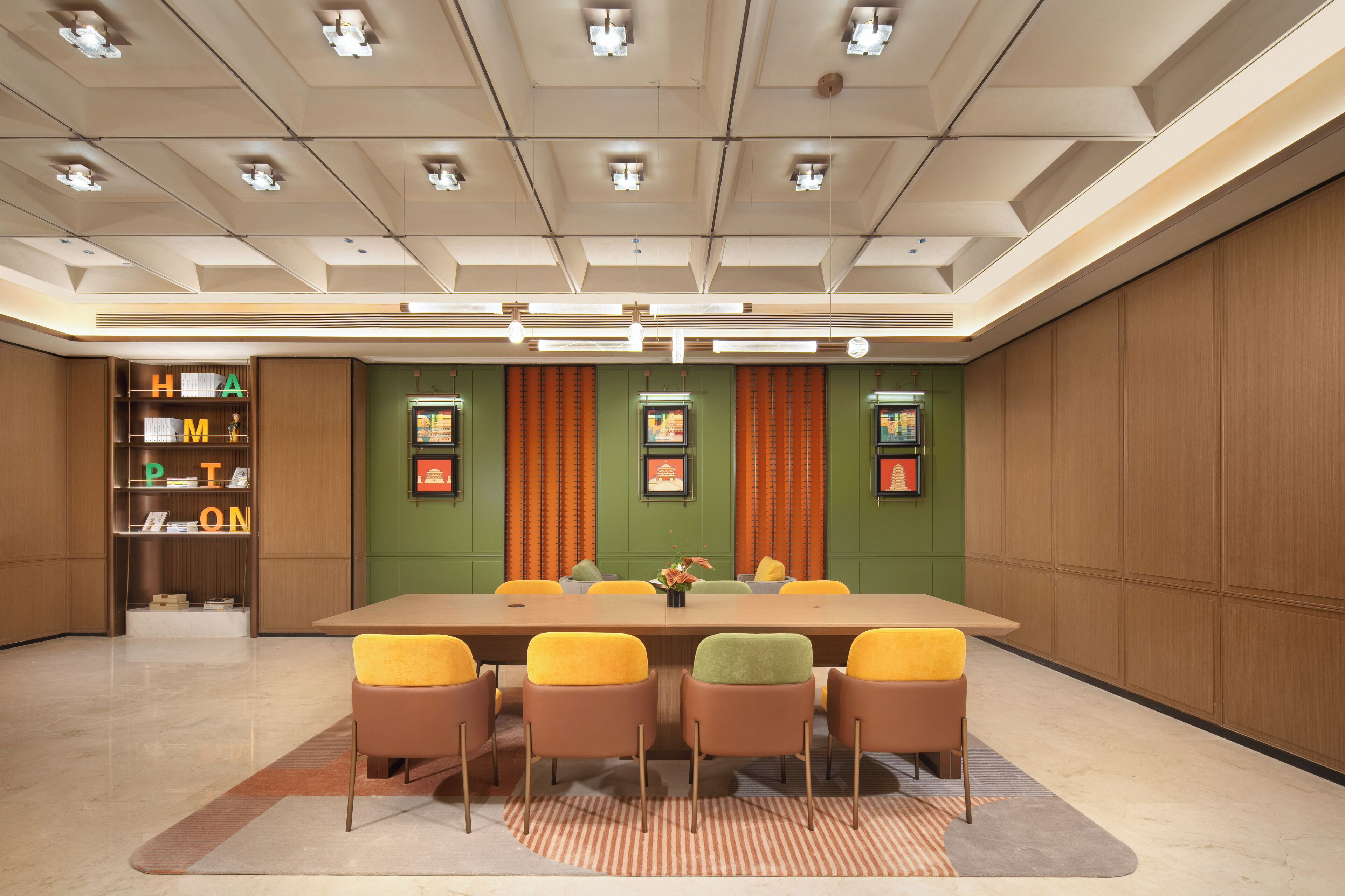A conference room with a long table, six chairs, a bookshelf, and framed pictures on the walls.