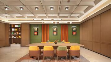A conference room with a long table, six chairs, a bookshelf, and framed pictures on the walls.