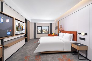 Une chambre d’hôtel moderne dotée d’un grand lit, d’une télévision, d’une vue sur la ville et d’un bureau avec une lampe.