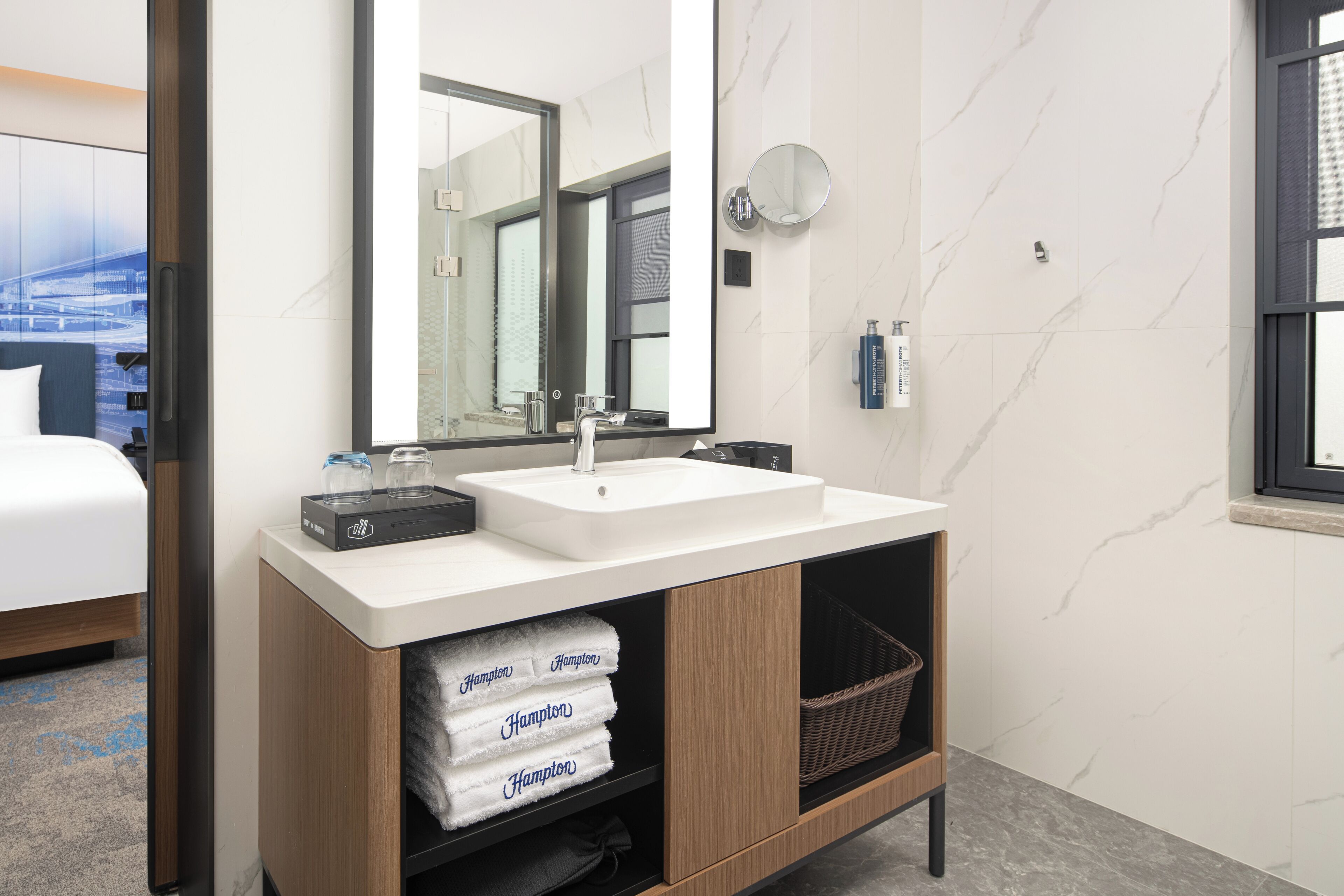 A modern bathroom with a large mirror, white sink, and wooden vanity.