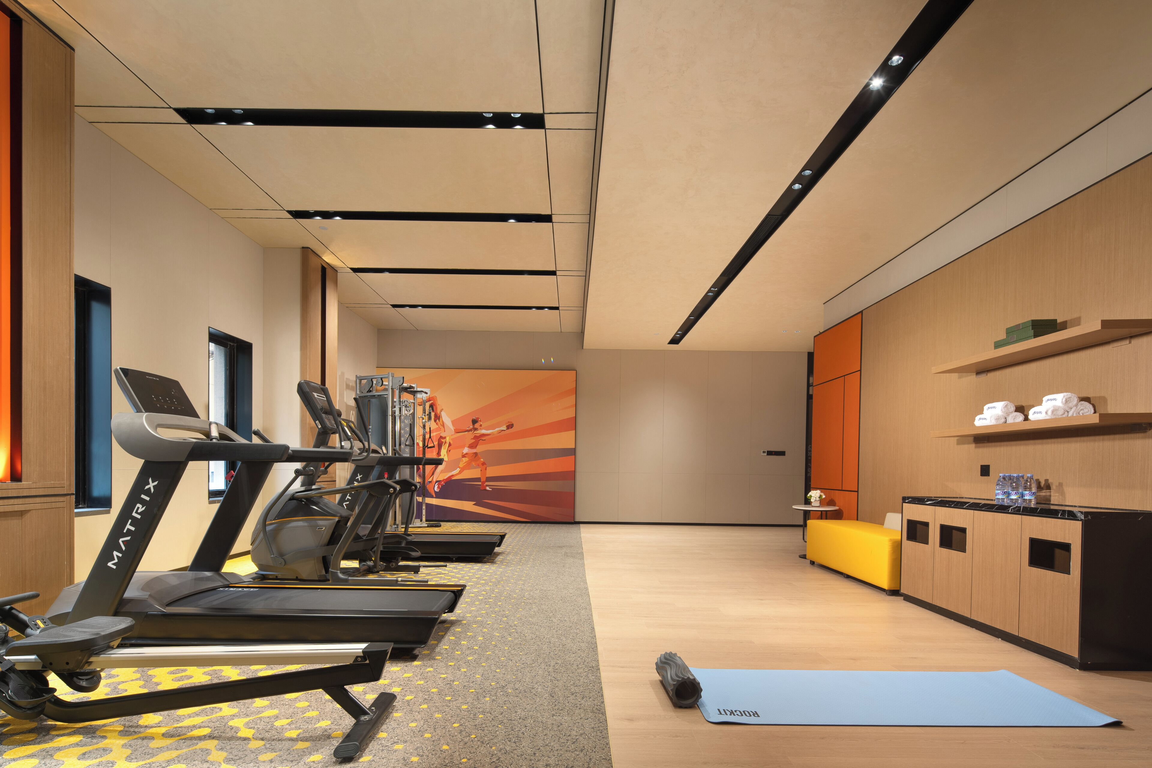 Un gimnasio con cintas de correr, una colchoneta de yoga y una pared con un cartel motivacional.