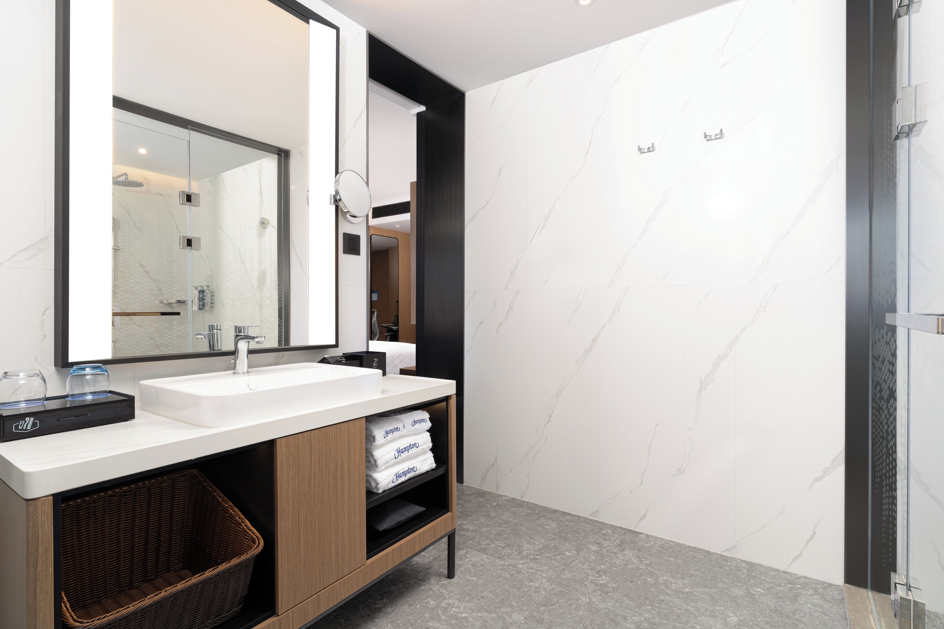 Un baño moderno con un espejo grande, dos lavabos, una ducha y una cesta de mimbre.