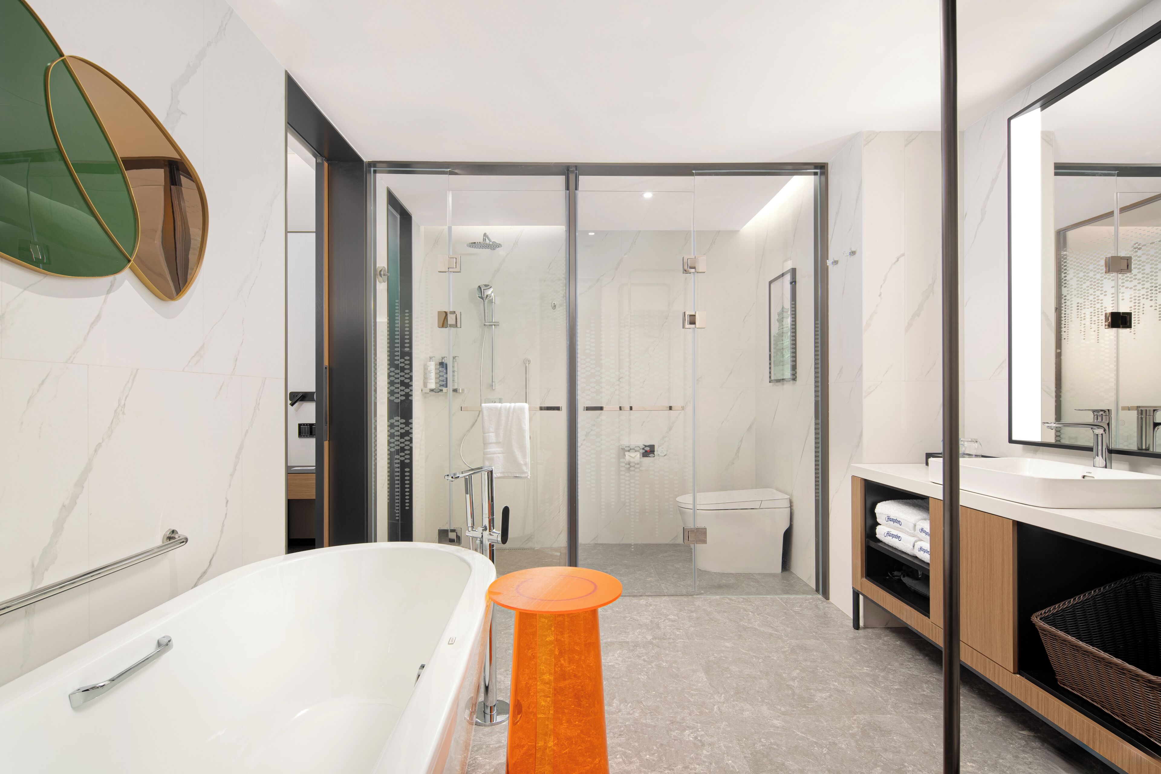 A modern bathroom with a bathtub, shower, and toilet, featuring marble walls and a glass shower enclosure.
