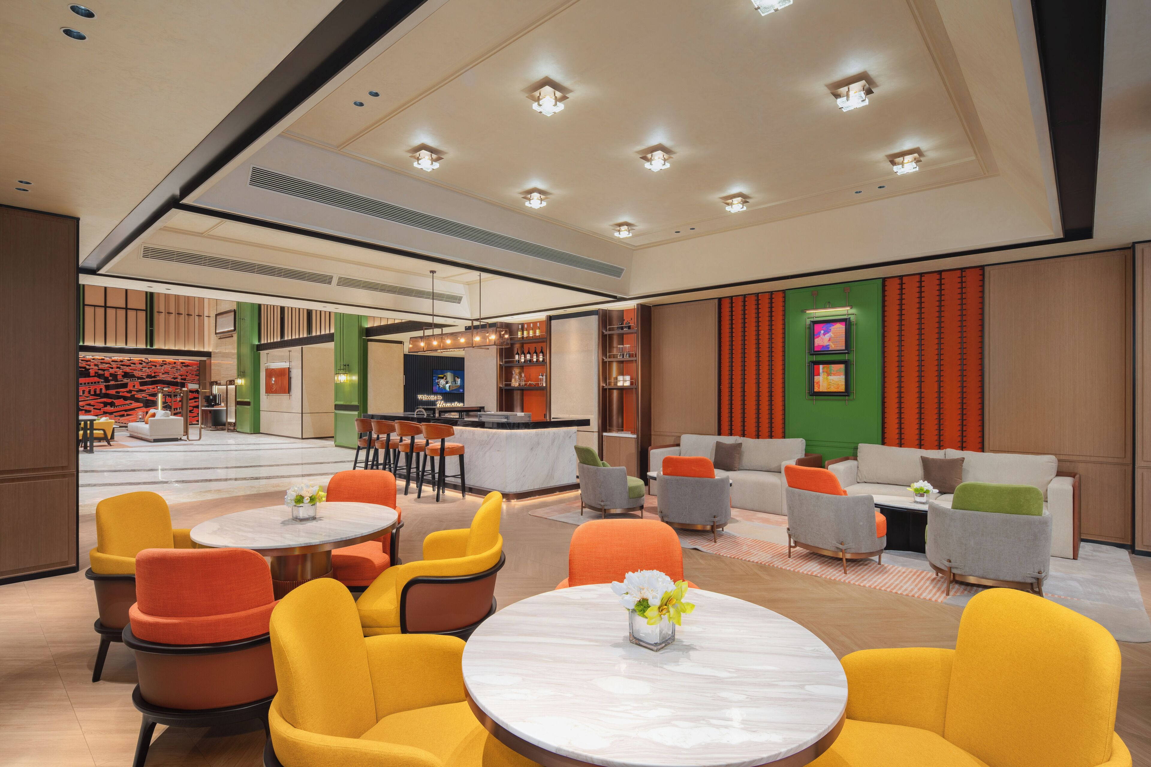 Een moderne lobby met ronde tafels, kleurrijke stoelen, een bar en een televisiescherm.