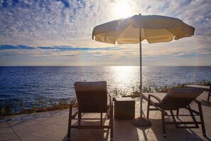 A seaside patio with two lounge chairs and a table, an umbrella, and a view of the ocean. - Holiday apartment mit Terrasse (Musalež)
