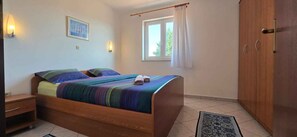 A bedroom with a wooden bed, a nightstand, a wardrobe, a window with curtains, and wall-mounted lights. - Holiday apartment mit Terrasse (Musalež)