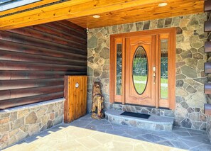 A wooden exterior with a stone wall, a wooden door with glass panels, and a bear sculpture. - 8RR Log Home w/ Spa Bath, Game Loft, AC, Great Yard Near Bretton Woods, Franconia Notch (Twin Mountain)