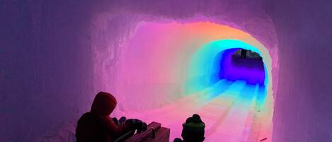 An ice tunnel with a wooden bench and a child sledding down a slope.