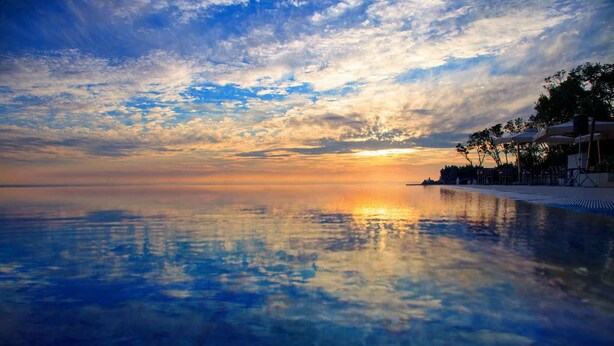 Une piscine à débordement aux eaux paisibles, reflétant un coucher de soleil, avec un ciel dégagé et un horizon lointain.