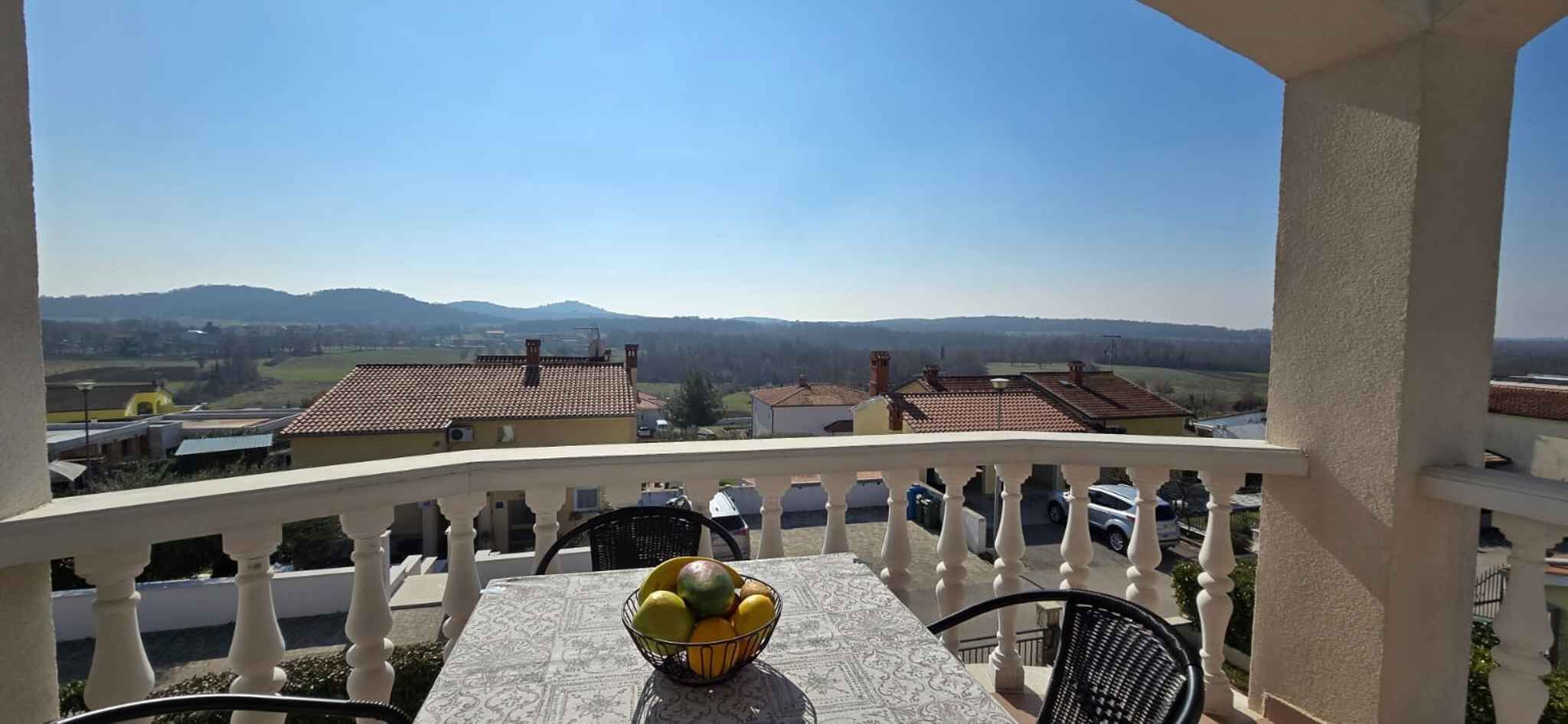 Ein Balkon mit Tisch und Stühlen, einer Obstschale und Blick auf Häuser und Berge.