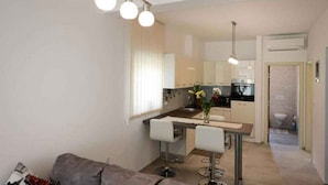 A modern kitchen with white cabinets, a dining area with a table and chairs, and a small bar area. - Holiday apartment with shared pool (Poreč)