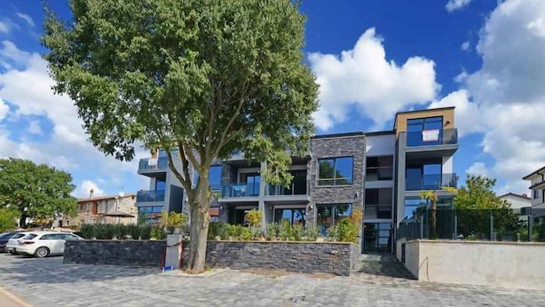 A modern multi-story building with a stone facade, large windows, and a parking area with cars. - Holiday apartment with shared pool (Poreč)