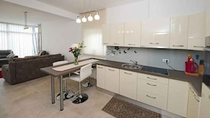 A modern kitchen with white cabinets, a dining area with a table and chair, and a living room with a sofa. - Holiday apartment with shared pool (Poreč)