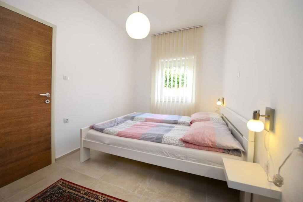 Een slaapkamer met een bed, nachtkastje, lamp, raam met zonwering, en een deur.