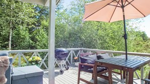 Um deck de madeira com mesa, cadeiras, churrasqueira e um grande guarda-sol.