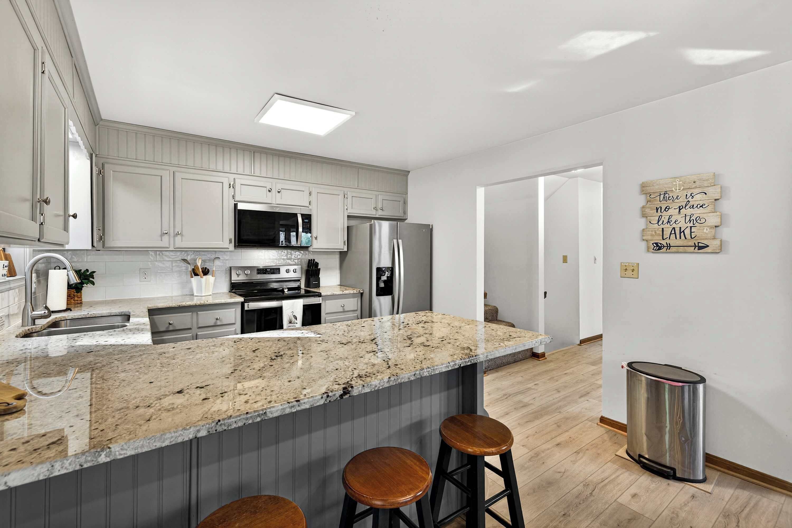 A modern kitchen with granite countertops, stainless steel appliances, and wooden bar stools.