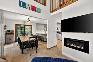 Una cocina moderna con armarios blancos, una zona de comedor con una mesa y sillas de madera, y una chimenea.