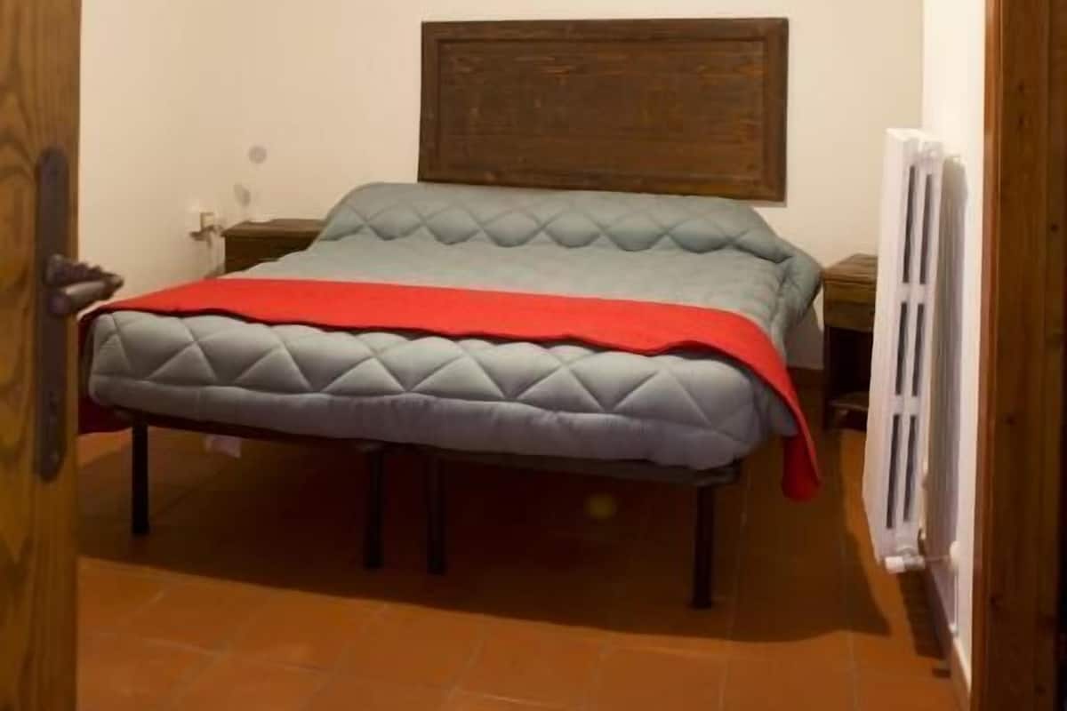 Une chambre à coucher comprenant un lit, une tête de lit en bois, une table de chevet, une commode, un luminaire suspendu et un radiateur.