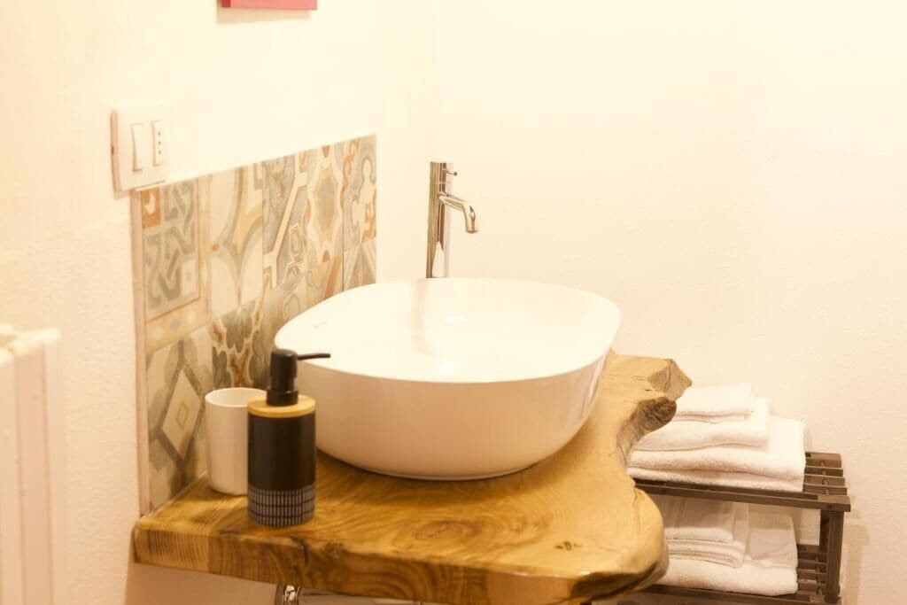 A bathroom with a white sink, a wooden countertop, a bottle of soap, and a towel rack.