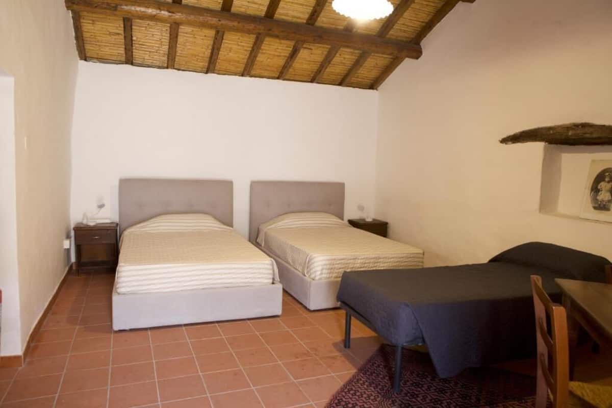 Une chambre avec deux lits, une petite table, une chaise, une table de chevet et un ventilateur de plafond.