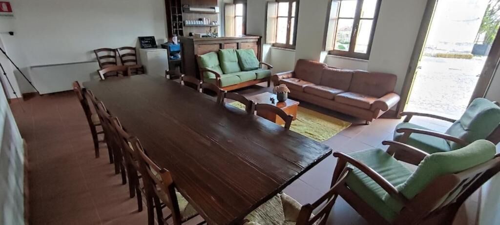 A spacious room with a large wooden dining table surrounded by chairs, a green sofa, and a red sofa.