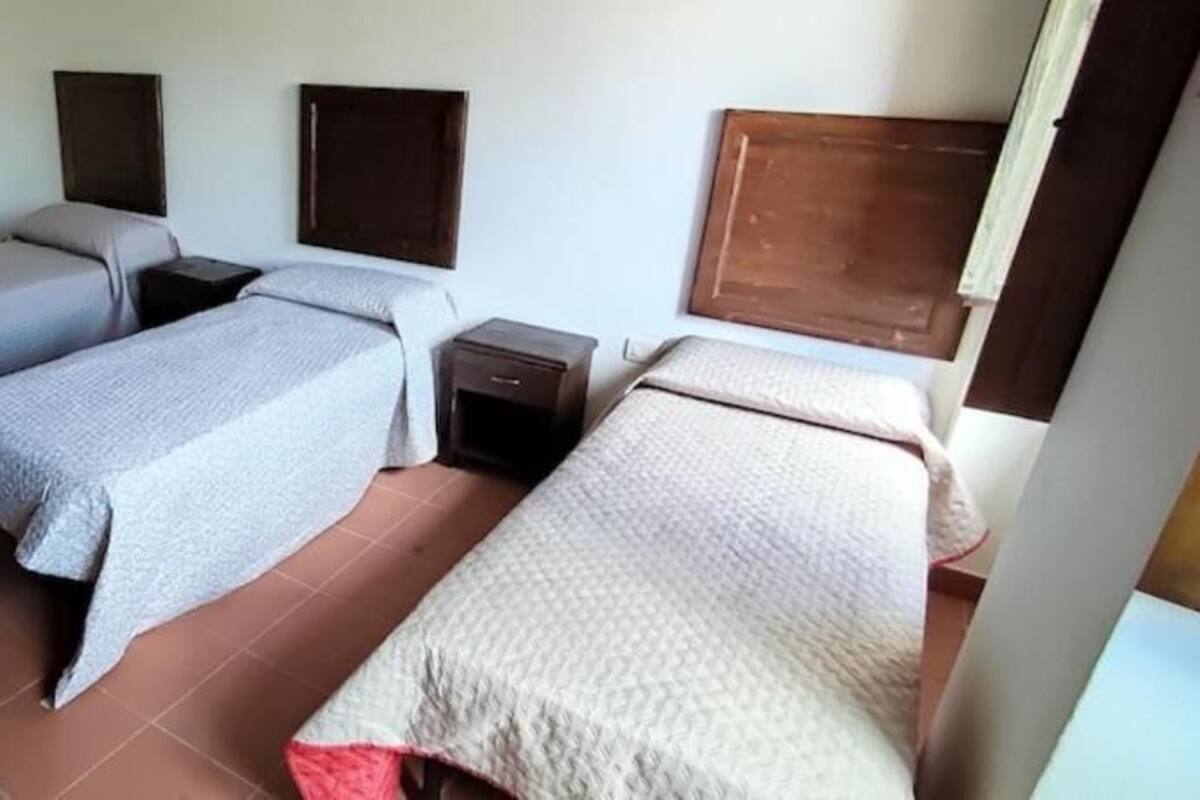 Une chambre avec trois lits simples, chacun doté d’une table de chevet, d’une tête de lit en bois et d’une fenêtre.