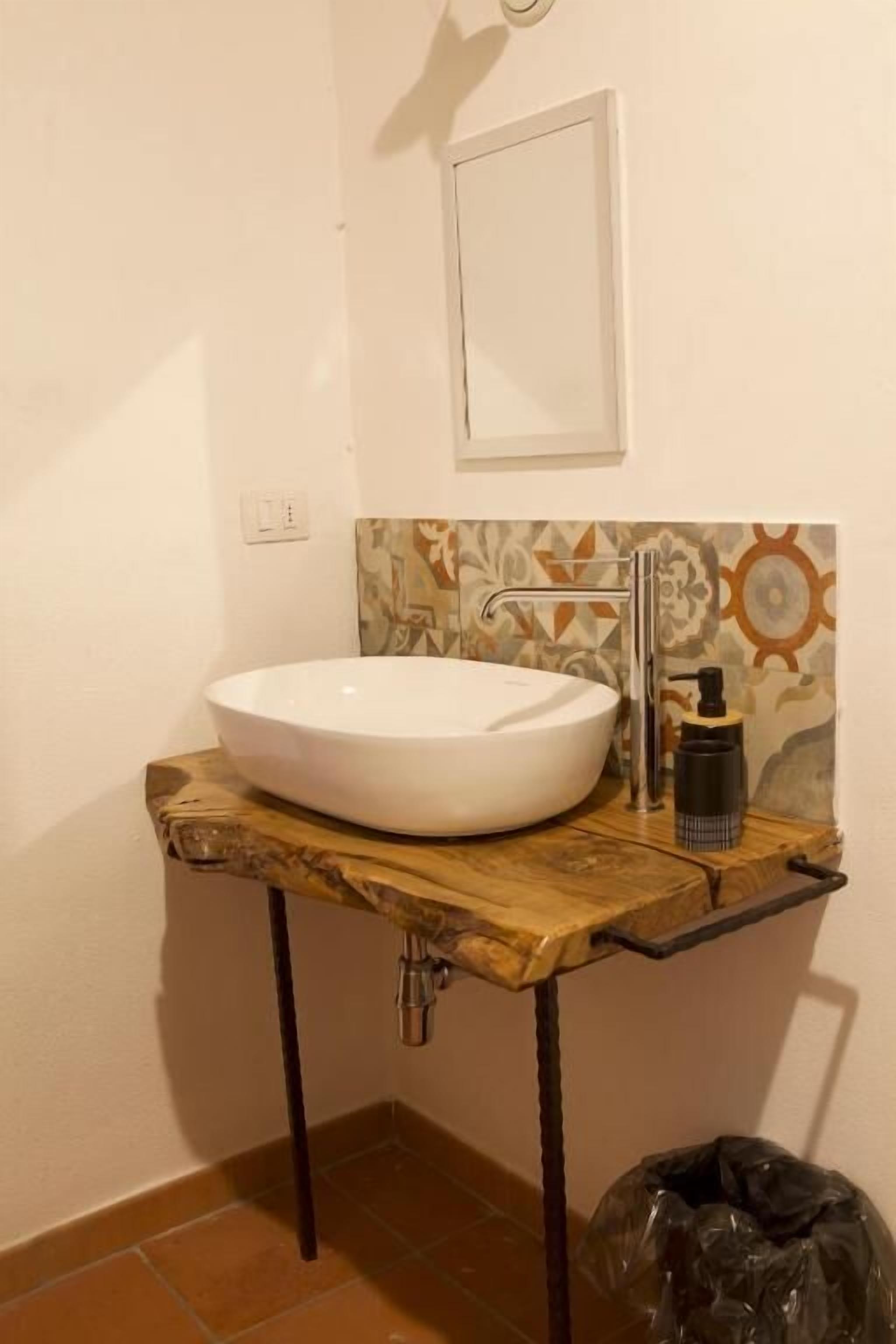 Un baño con lavamanos blanco, encimera de madera y salpicadero de azulejos estampados.