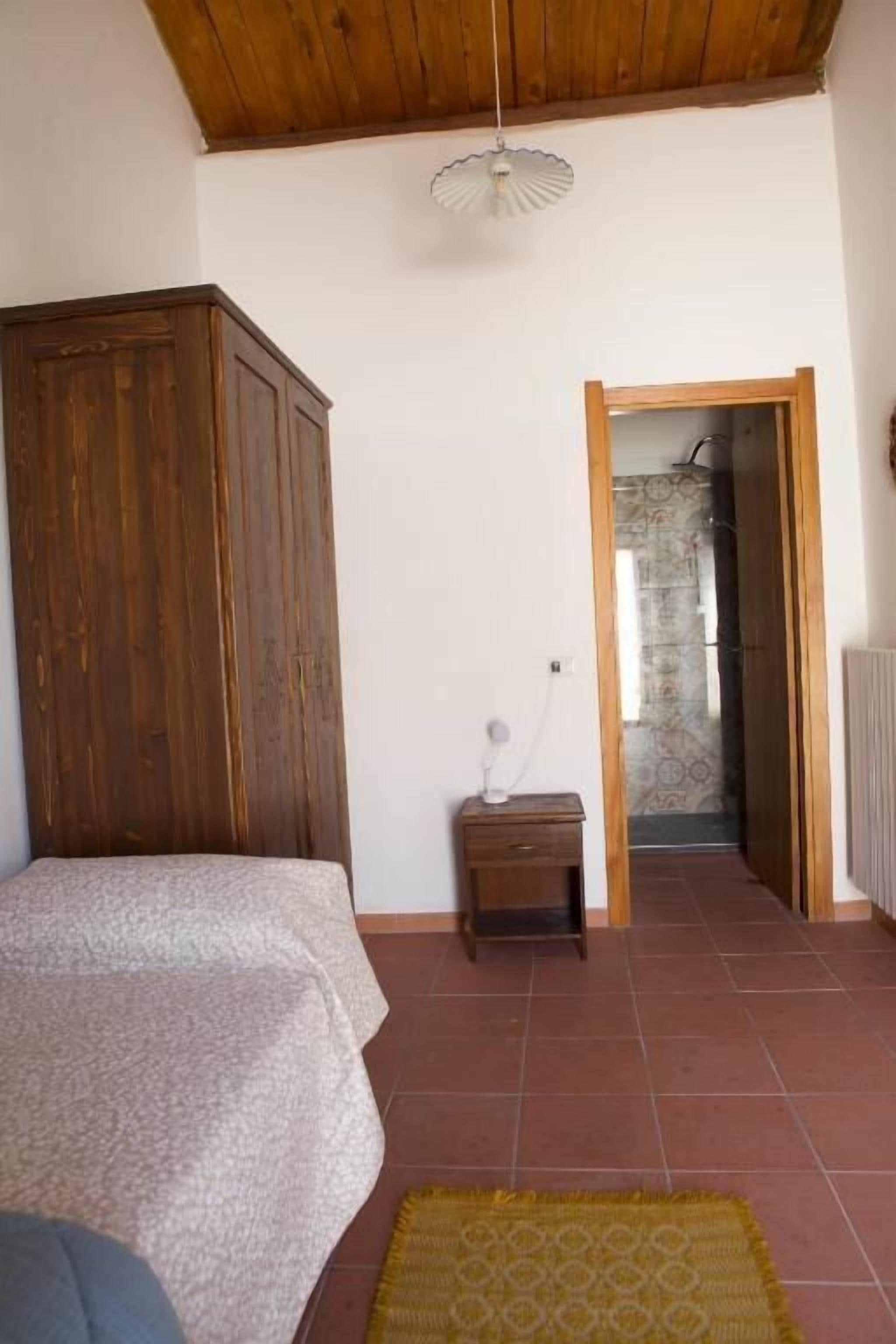 A bedroom with a wooden wardrobe, a bed, a small bedside table, and a radiator.