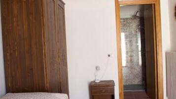 A bedroom with a wooden wardrobe, a bed, a small bedside table, and a radiator.