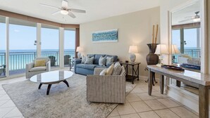 A spacious living area with a balcony, a ceiling fan, a blue sofa, a striped armchair, and a coffee table. - 3 Bedroom in Aqua Resort! 811 Renovated with Gorgeous Views!  New listing (Panama City Beach)