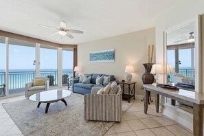 A spacious living area with a balcony, a ceiling fan, a blue sofa, a striped armchair, and a coffee table. - 3 Bedroom in Aqua Resort! 811 Renovated with Gorgeous Views!  New listing (Panama City Beach)