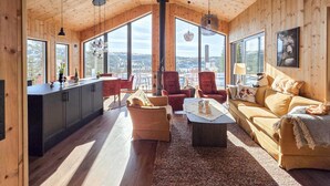Amplia habitación con cocina, comedor y sala de estar, con ventanas grandes y paredes de madera.