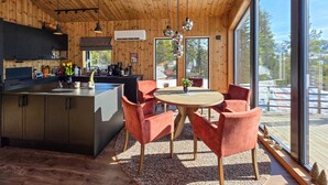 Una cocina moderna con una isla central, sillas rojas alrededor de una mesa de madera y ventanas amplias que dan al exterior.