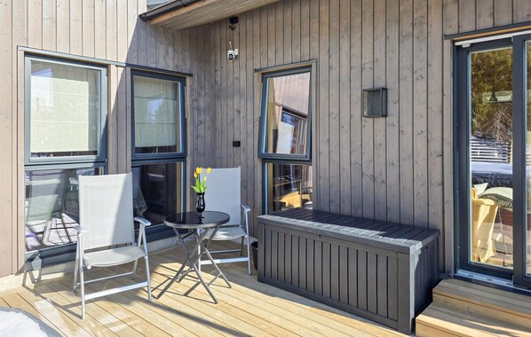 Eine Terrasse mit Tisch und Stühlen, eine kleine Sitzecke mit einer Bank und große Fenster.