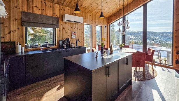 Una cocina moderna con una isla grande, paredes de madera y ventanas amplias que ofrecen vistas a un paisaje urbano.