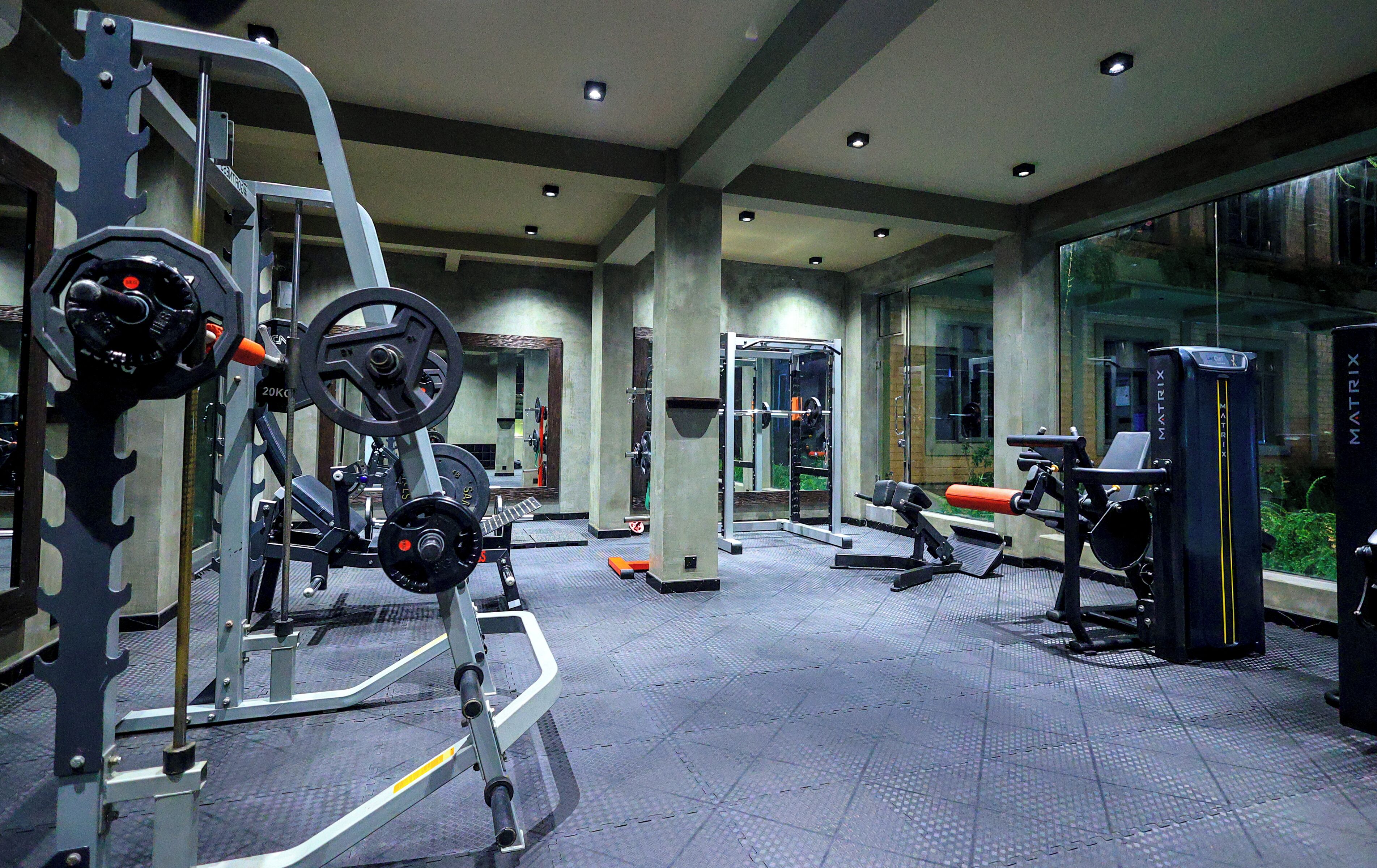 A gym with various exercise equipment, a mirrored wall, and a view of the outside.