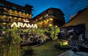A hotel with a prominent illuminated sign, outdoor seating area, and a decorative rock garden. - Arama Transit Hotel  (Katunayake)