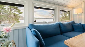 A blue sofa facing a window with a view of a lake and trees. - Nice home in Risør with house sea view (Risør)