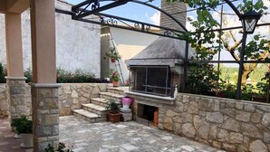 Eine Terrassengaststätte mit Steinboden, Grill, Topfpflanzen und einer Steinmauer.