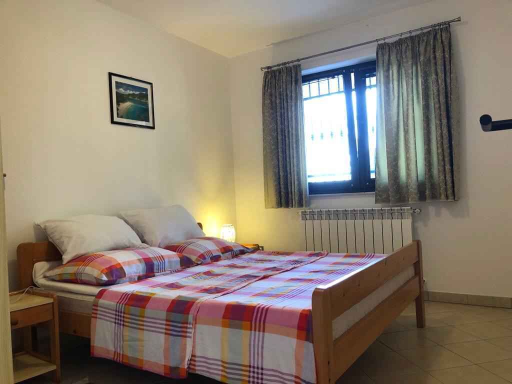 Un dormitorio con cama, mesita de noche, ventana con cortinas, radiador y un cuadro colgado en la pared.