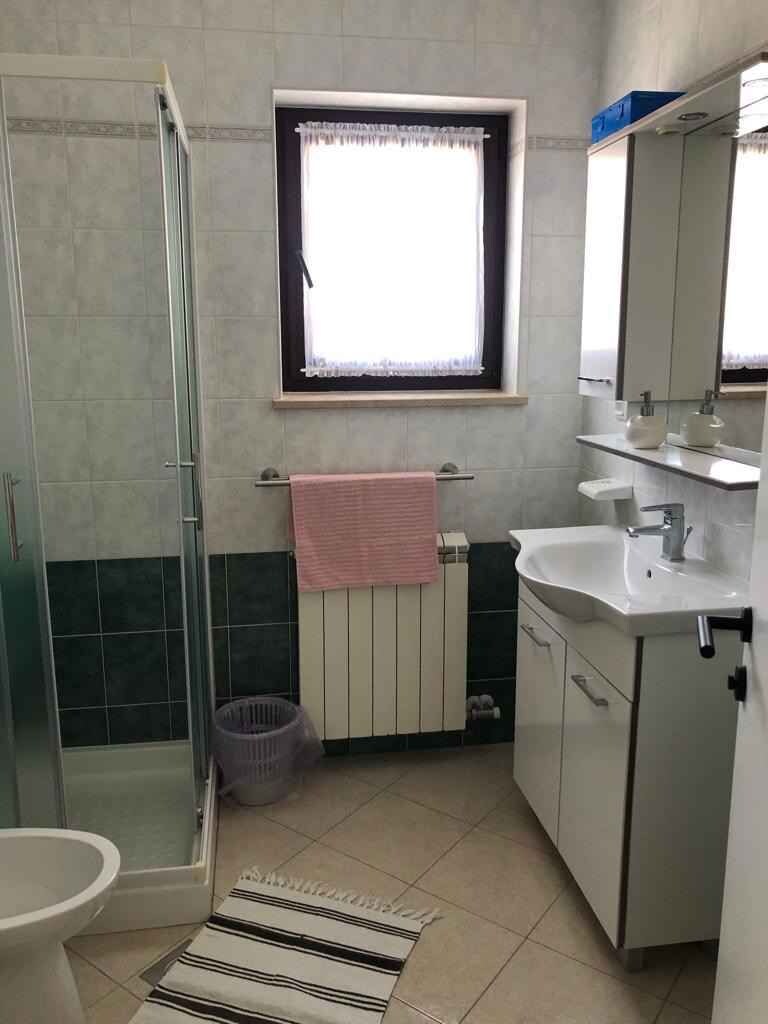 A bathroom with a shower, a sink, a toilet, a window, and a radiator.
