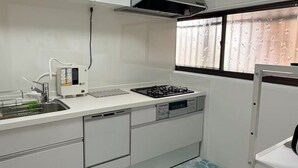 Una cocina compacta con armarios blancos, estufa a gas, lavavajillas y una ventana con vidrio esmerilado.