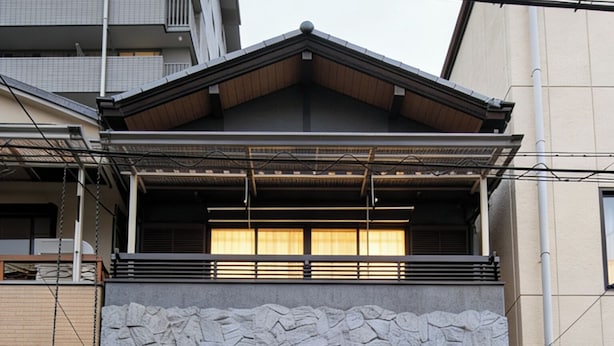 Un edificio residencial de dos pisos con un balcón de madera, fachada de piedra y una entrada tradicional japonesa.