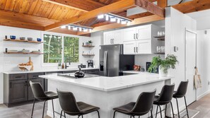 A modern kitchen with a large island, bar stools, white cabinetry, and a wooden ceiling.